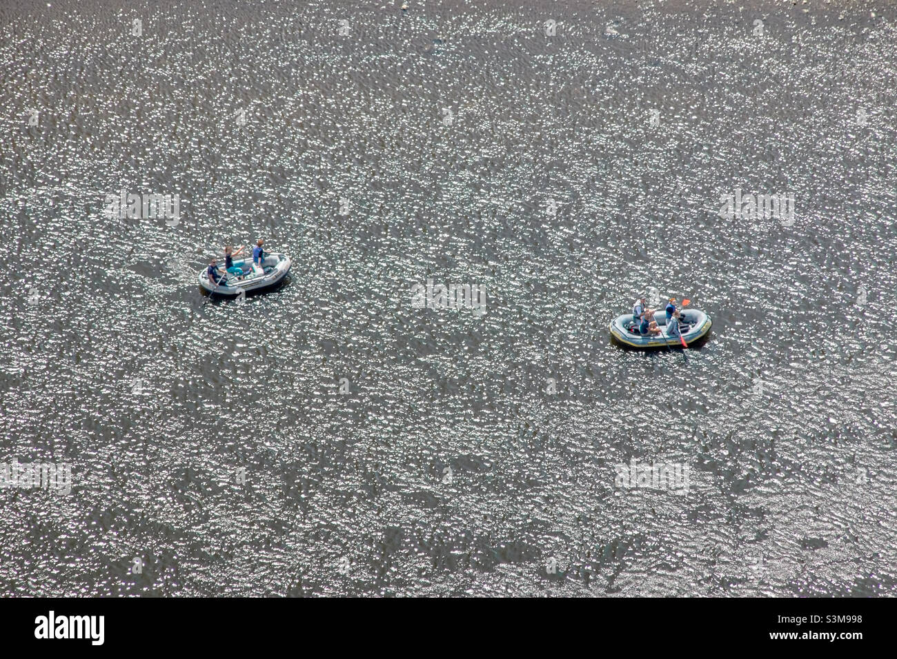 Two grey rubber dinghies on the water with three and four people near