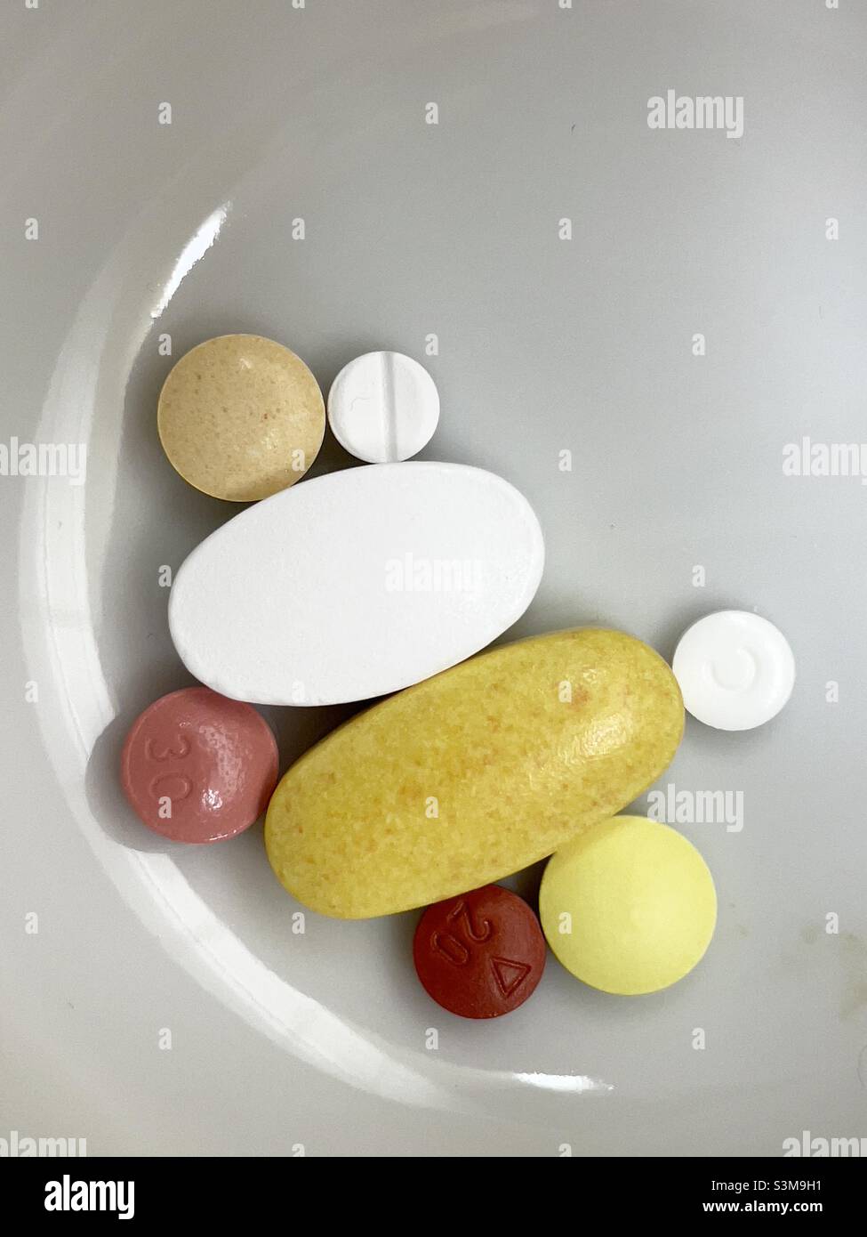An assortment of pills round and oval in a small white ceramic bowl - Smartphone Captured Stock Image