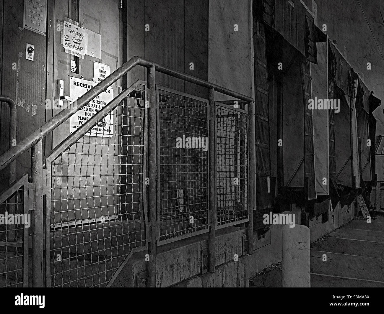 A newspaper’s post-press, shipping and receiving, dock area in black and white, with a  grunge effect overall and an added spotlight lighting effect on the truck driver entry. - Smartphone Captured Stock Image
