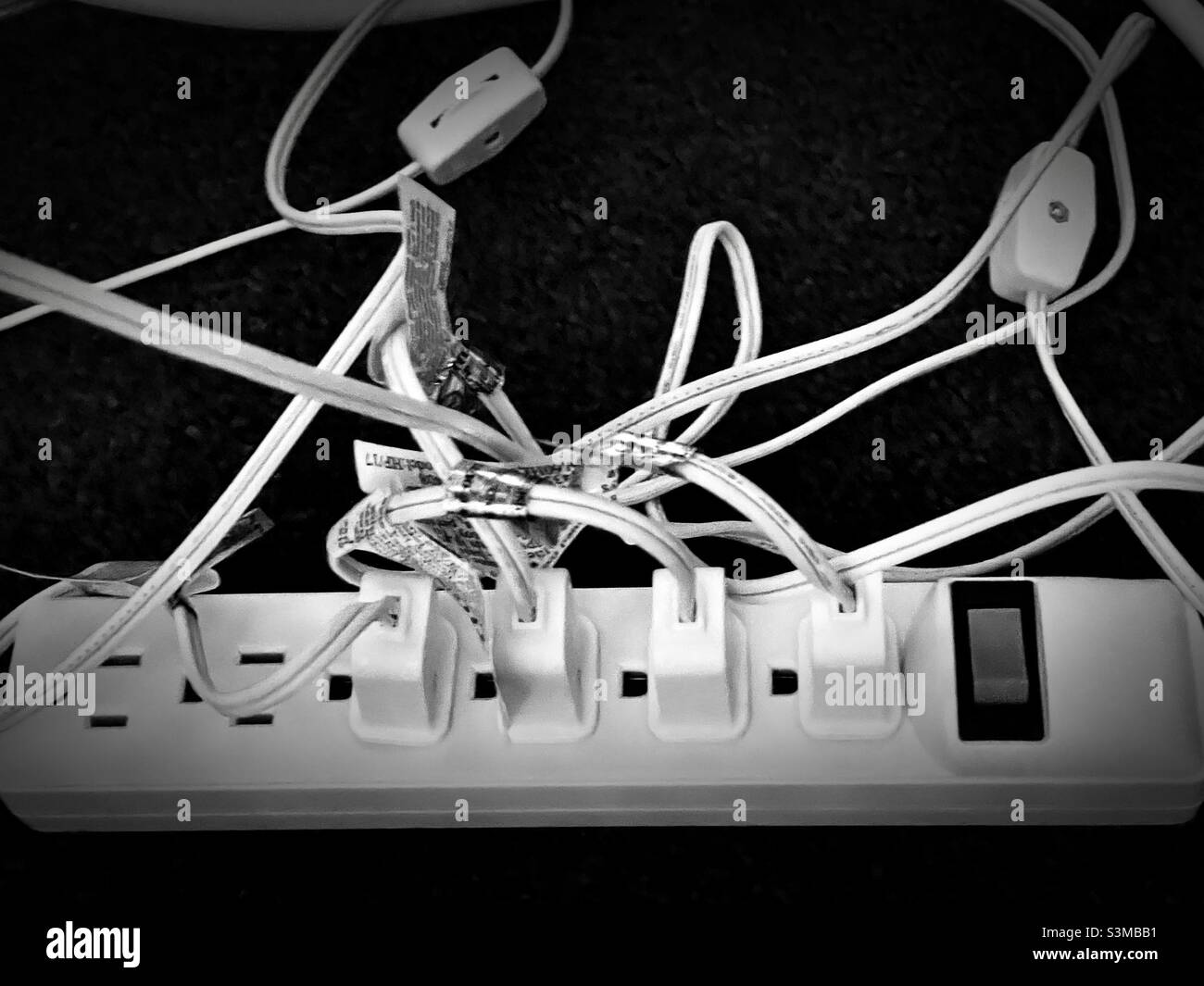 A power strip under a living room table has multiple plugs in its’ sockets during the Christmas season to accommodate all the lighted decorations. - Smartphone Captured Stock Image