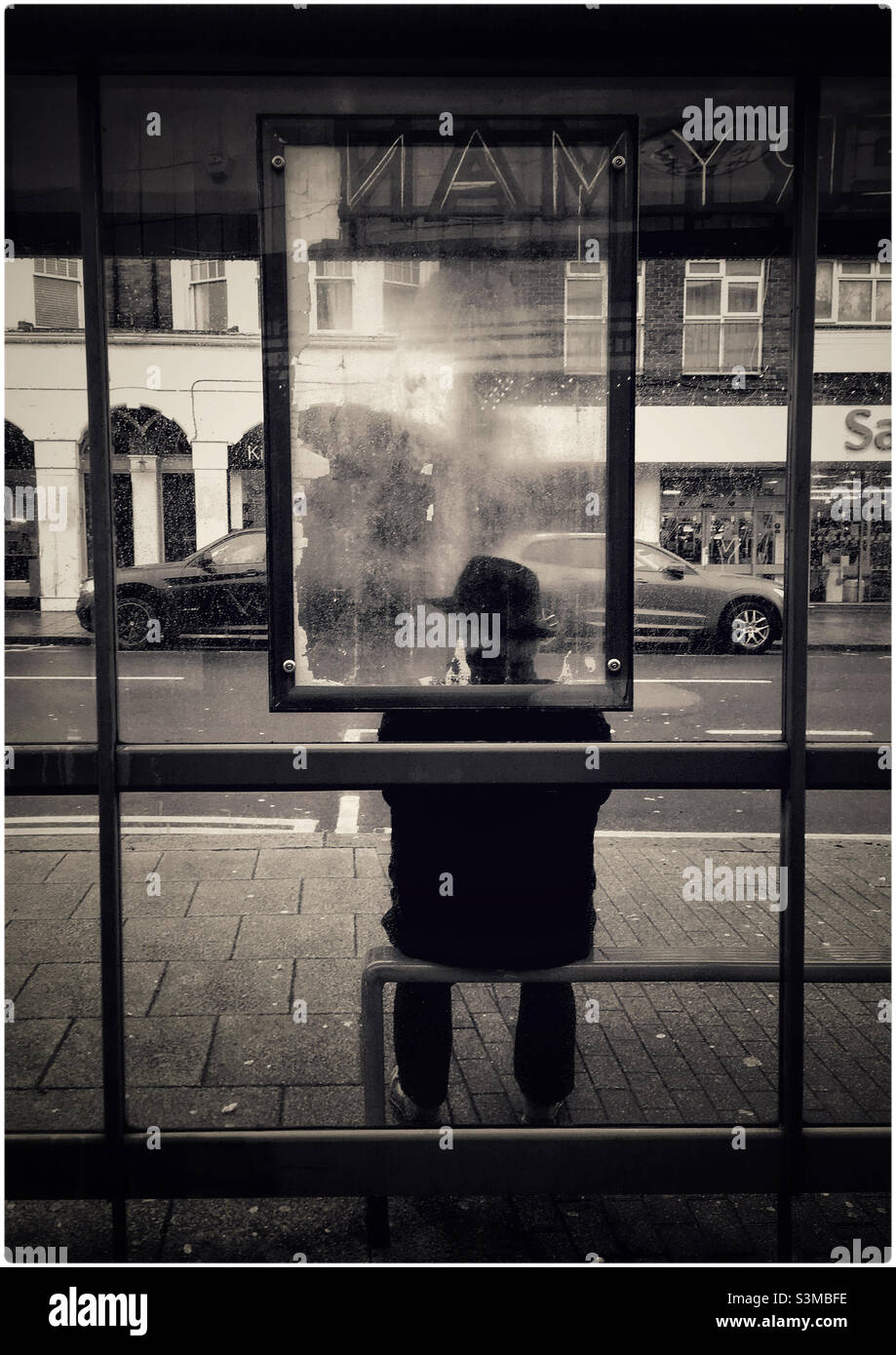 Man in hat waiting at a bus stop in Muswell Hill, north London - Smartphone Captured Stock Image