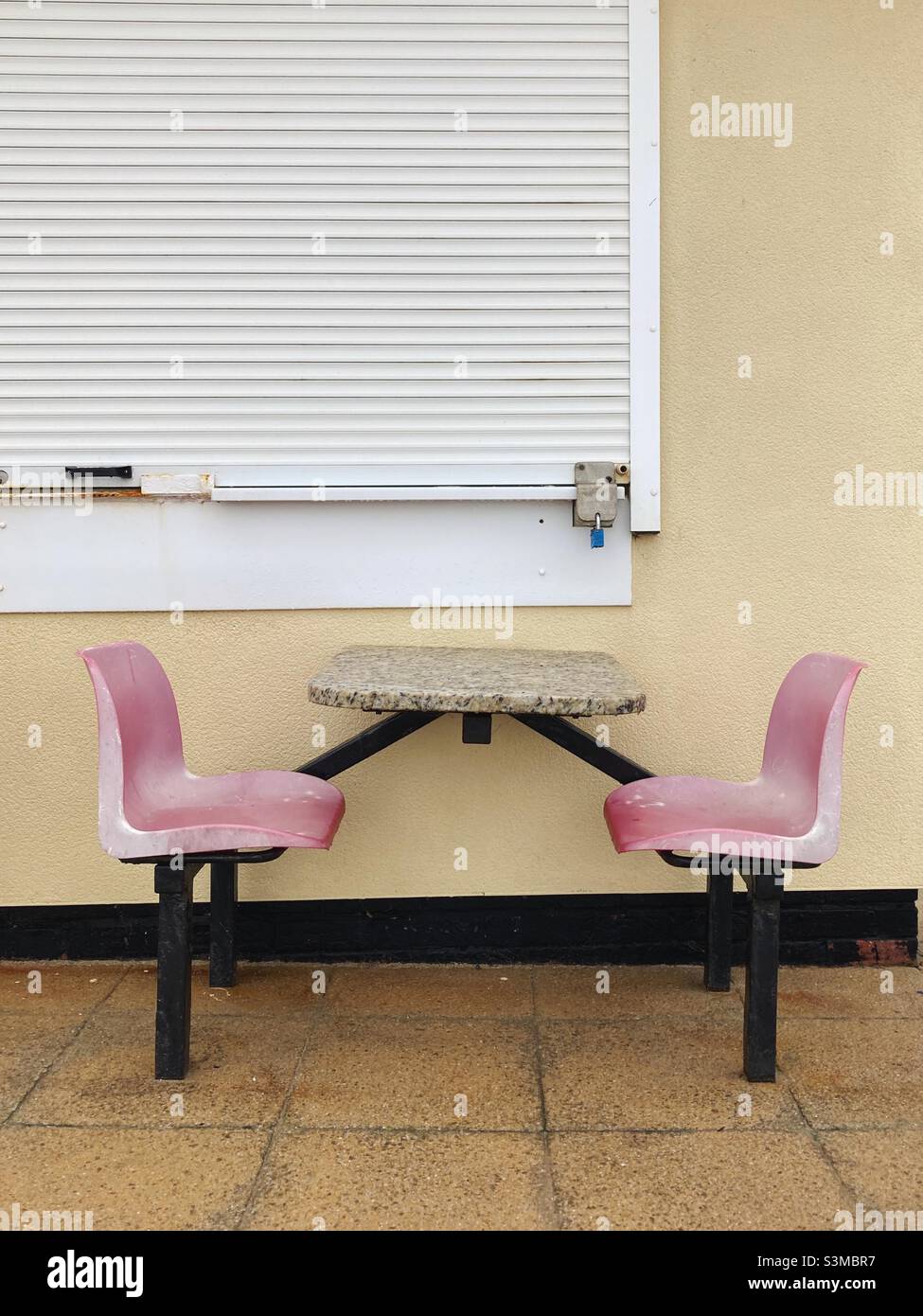 Faded seats at a table at a seaside café, closed for the winter - Smartphone Captured Stock Image