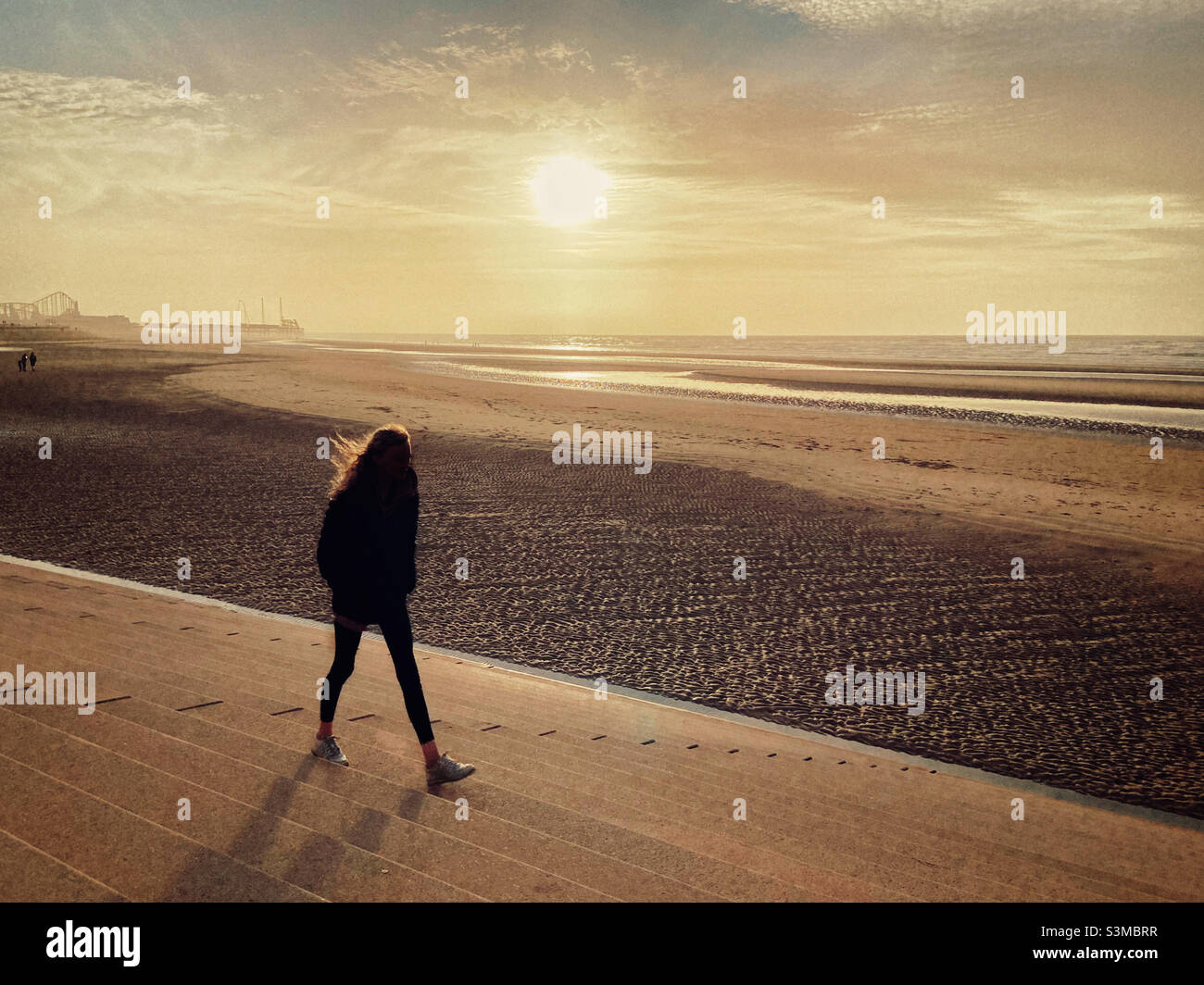Girl in silhouette walking on sea wall at Blackpool against a low winter sun Stock Photo