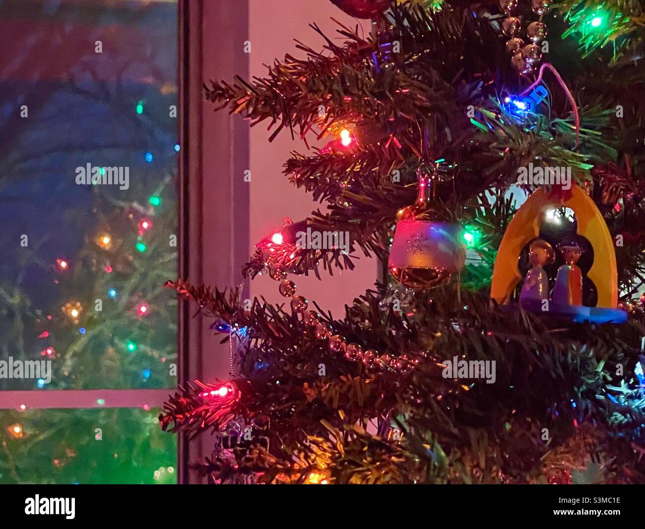 A home’s decorated and lighted Christmas tree is seen reflected in the window glass after dark in Utah, USA. - Smartphone Captured Stock Image