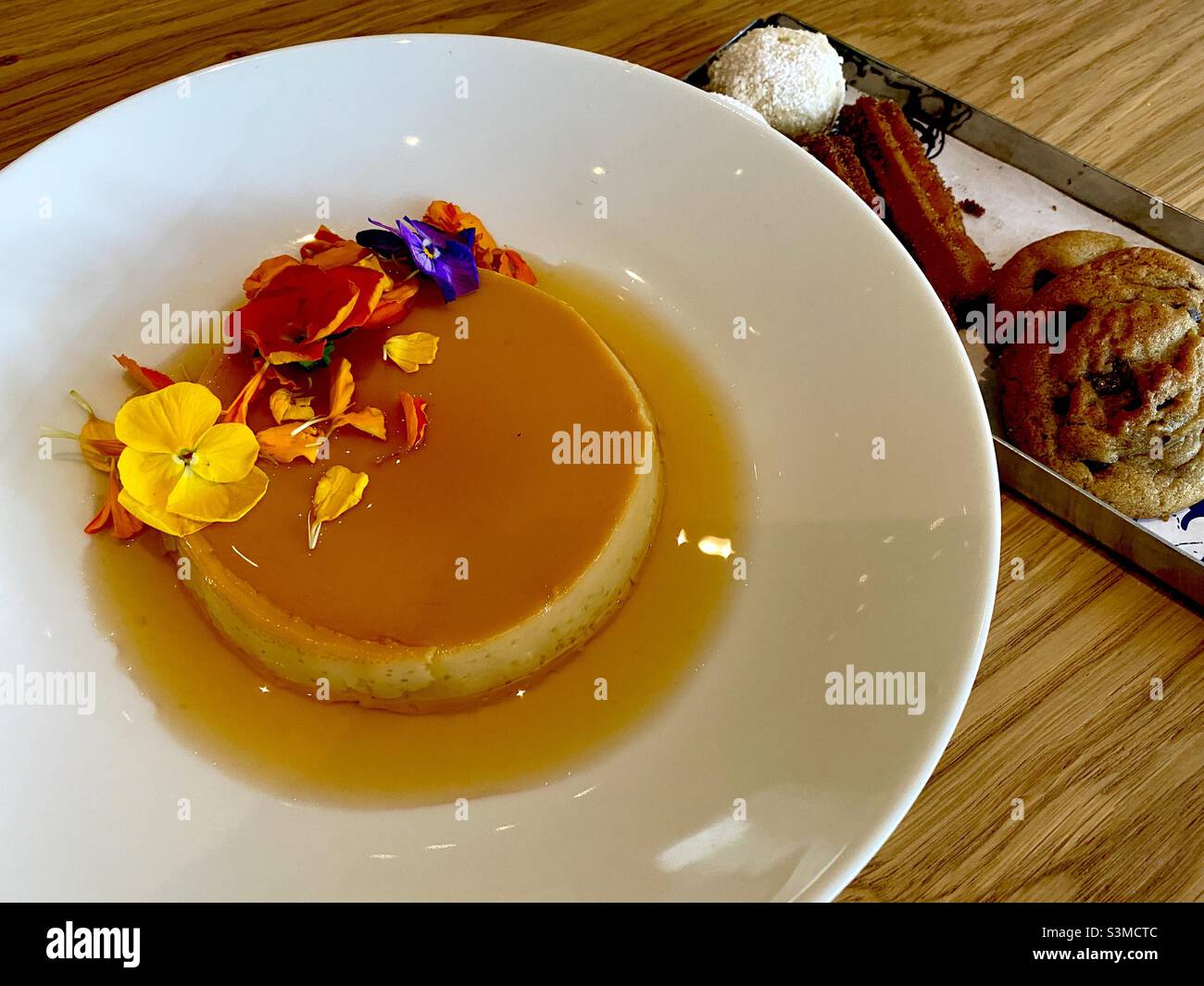 Mexican flan dessert with edible flowers and Mexican cookies on the side. - Smartphone Captured Stock Image