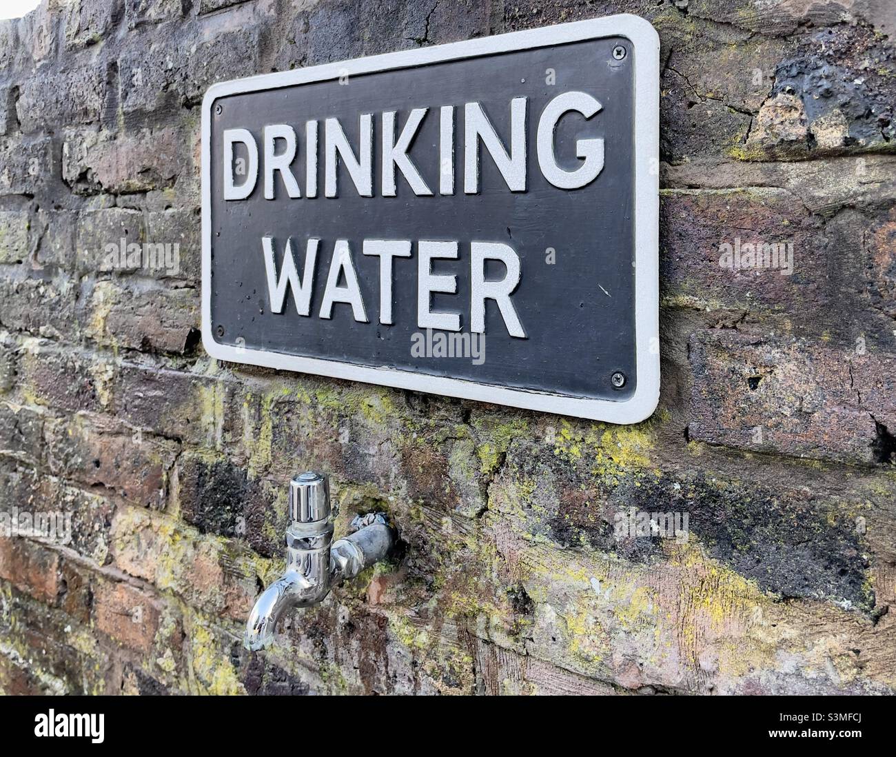 A tap protruding from a brick wall in Upton upon Severn with a notice above saying “drinking water”. - Smartphone Captured Stock Image