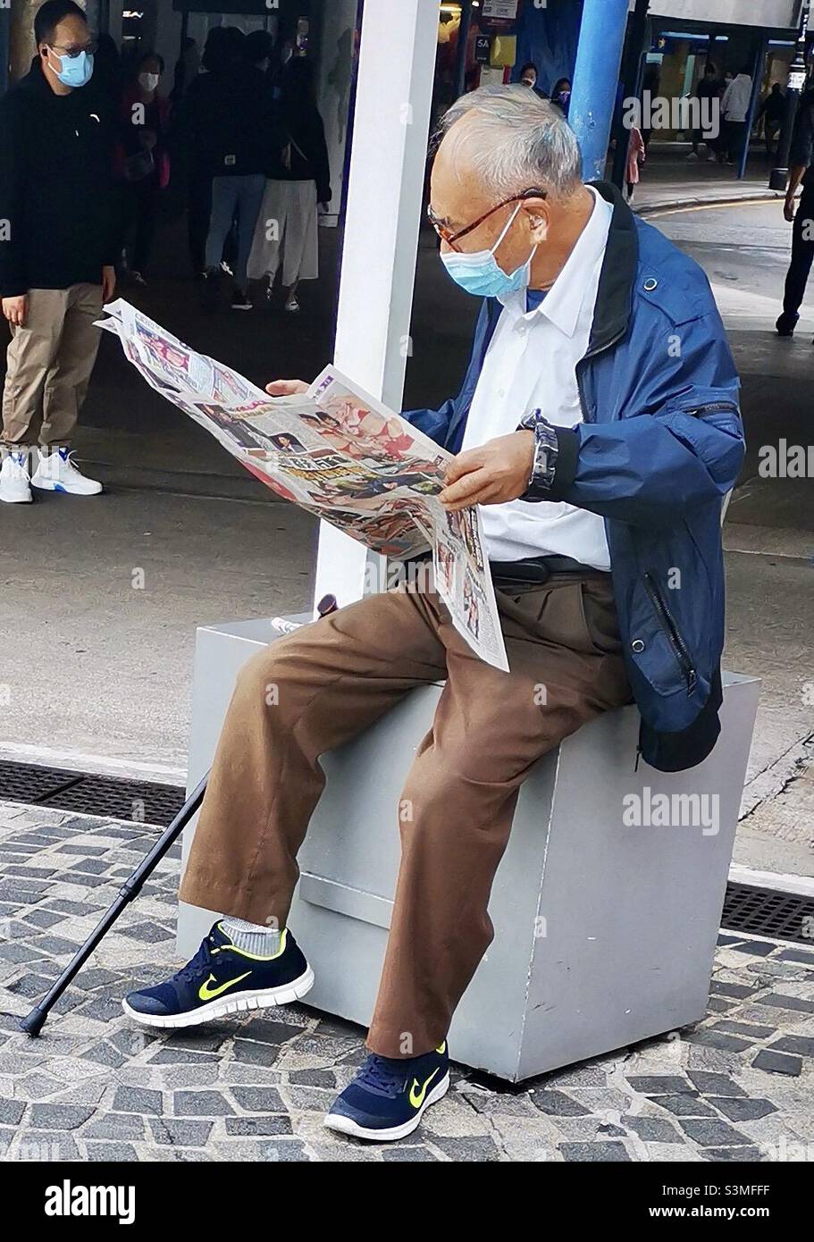 Reading the newspaper while wearing a surgical mask during the Covid-19 pandemic in Hong Kong. Stock Photo