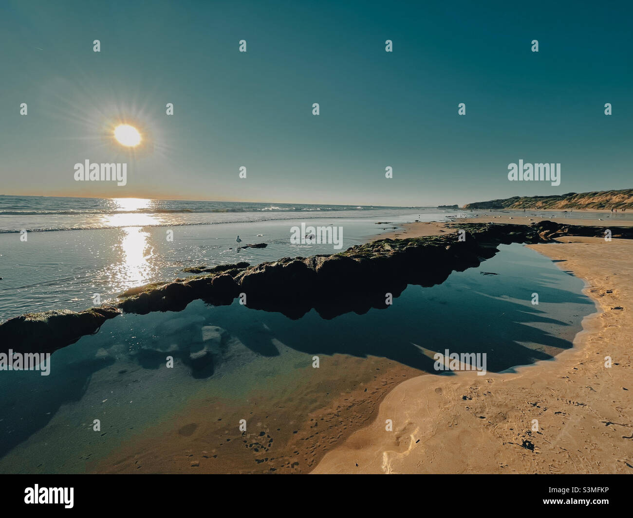 Sunny California beach at low tide with shadows reflecting in a tide