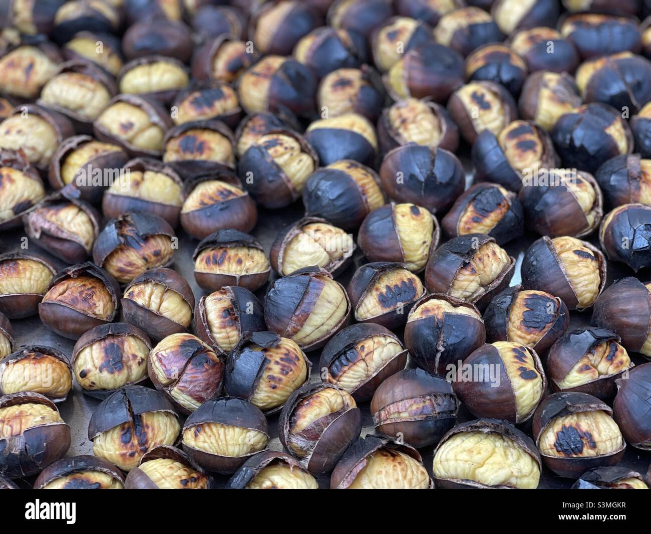 Many roasted chestnuts on a tray at a food market in Italy Stock Photo