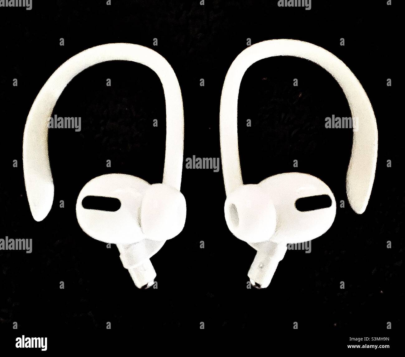 The newest pair of Apple AirPods Pro, with ear hooks attached, sitting on a dark background. - Smartphone Captured Stock Image