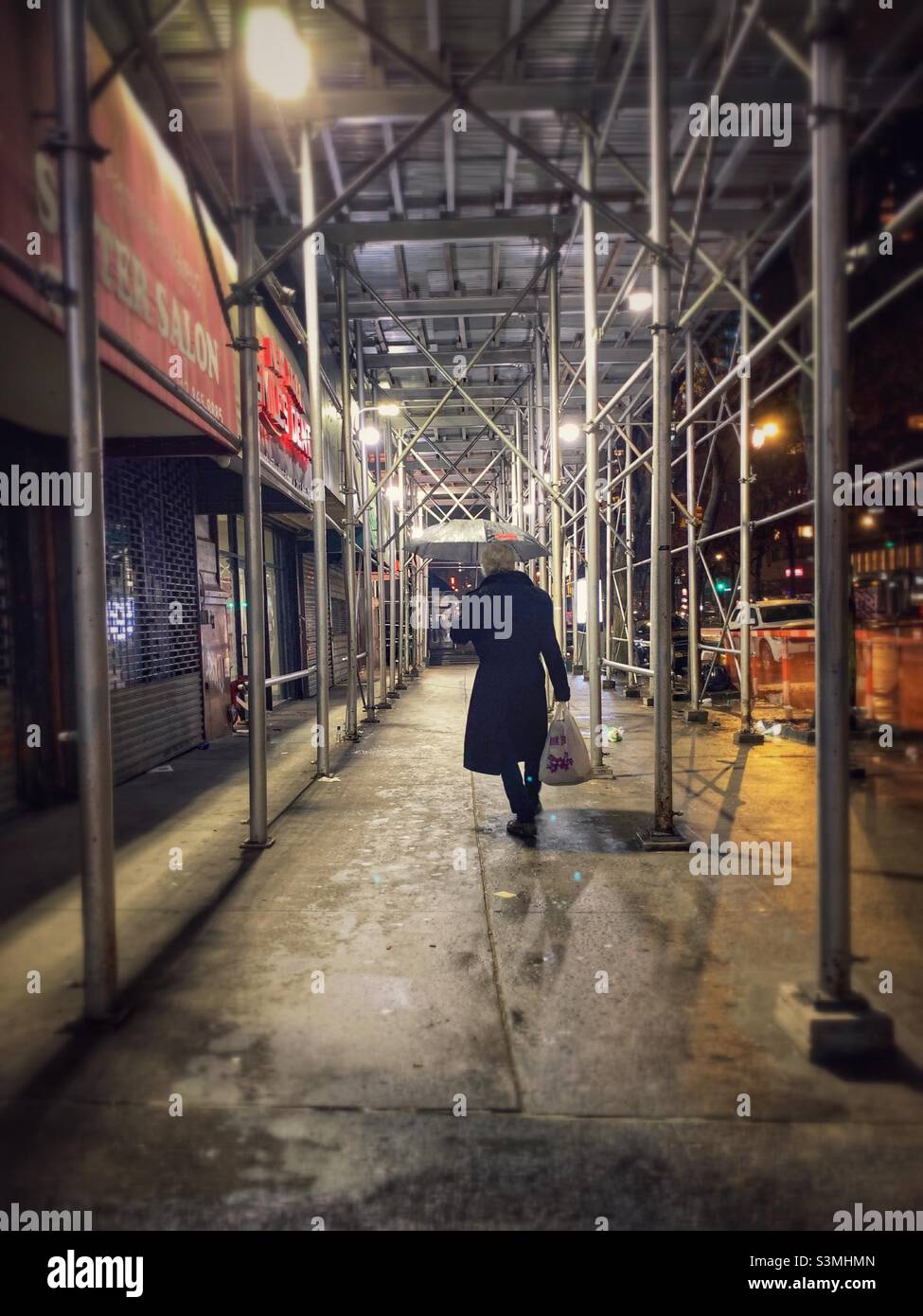 A walking man carrying a plastic bag and umbrella under the scaffolding. - Smartphone Captured Stock Image