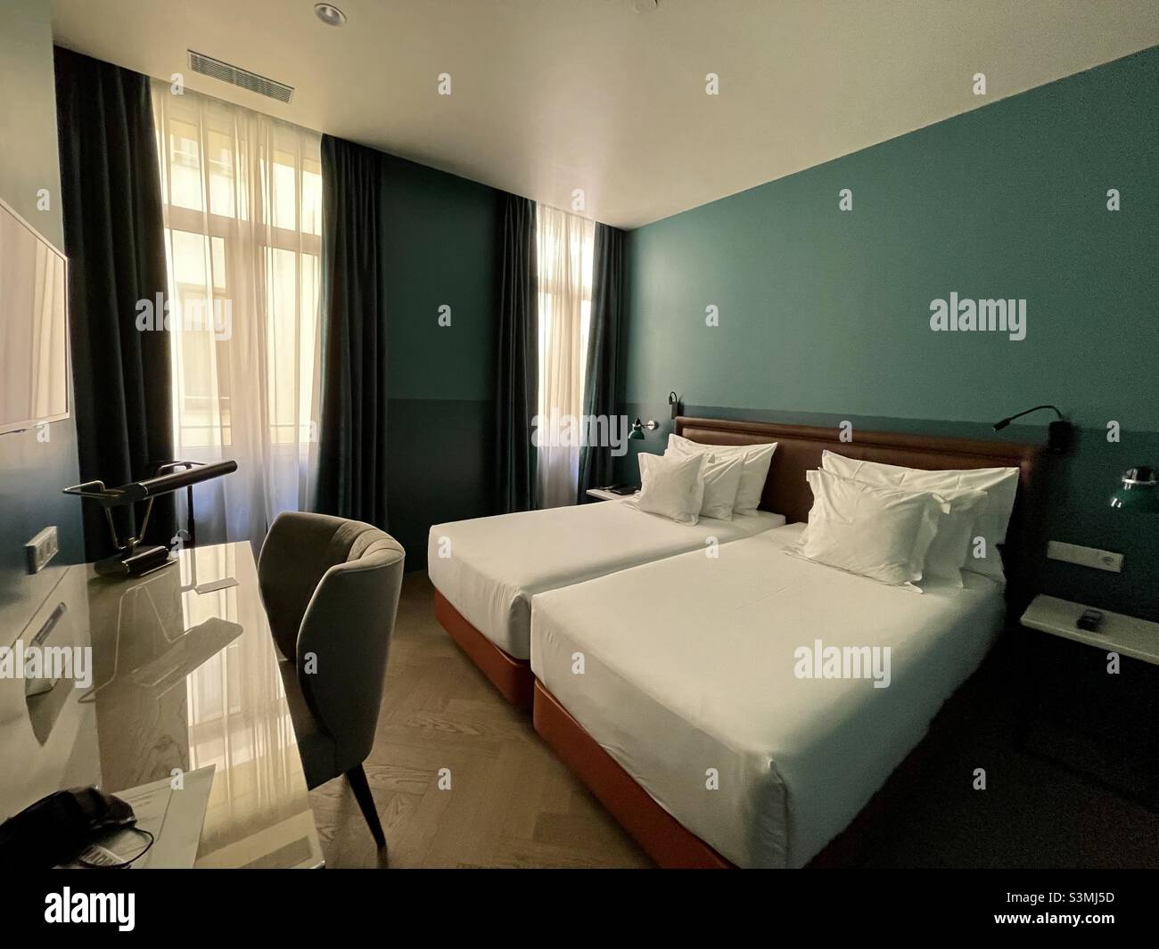 A beautiful hotel room with twin beds, white bedding, teal walls, a