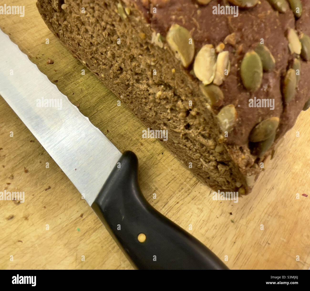 Half a loaf of brown bread studded with pumpkin seeds, together with a serrated bread knife - Smartphone Captured Stock Image