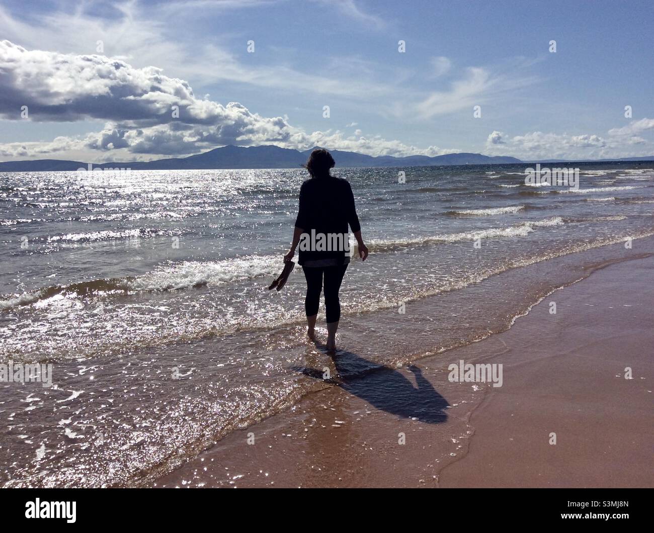 Silhouette and shadow of a woman paddling in the sea at Seamill Beach - Seamill, West Kilbride, North Ayrshire, Scotland Stock Photo