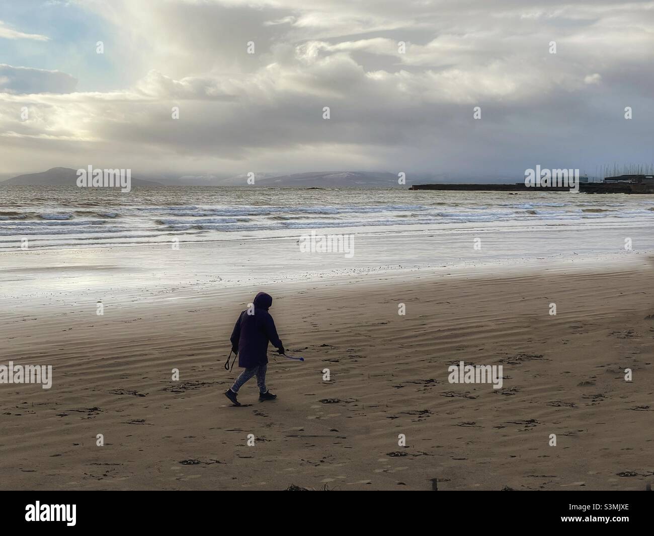 Lone elderly woman walking on wintery Scottish beach Stock Photo