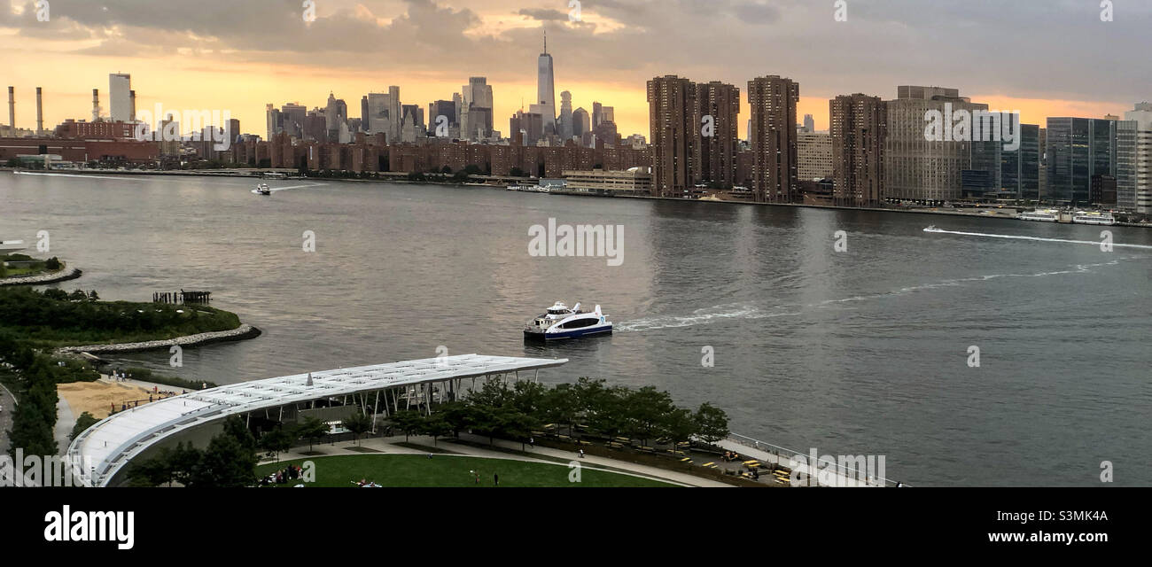 Vantage view of the East River and Midtown Manhattan and the East Village from Long Island City Hunters Point South Park at sunset. East River Ferry arriving to Hunters Point landing. Stock Photo