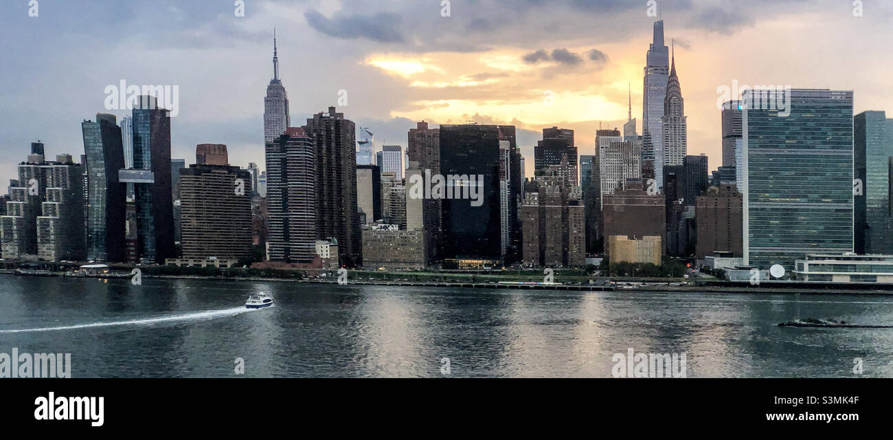 Vantage view of the East River and Midtown Manhattan and the East Village from Long Island City Hunters Point South Park at sunset. East River Ferry arriving to the 34th Street landing. Stock Photo