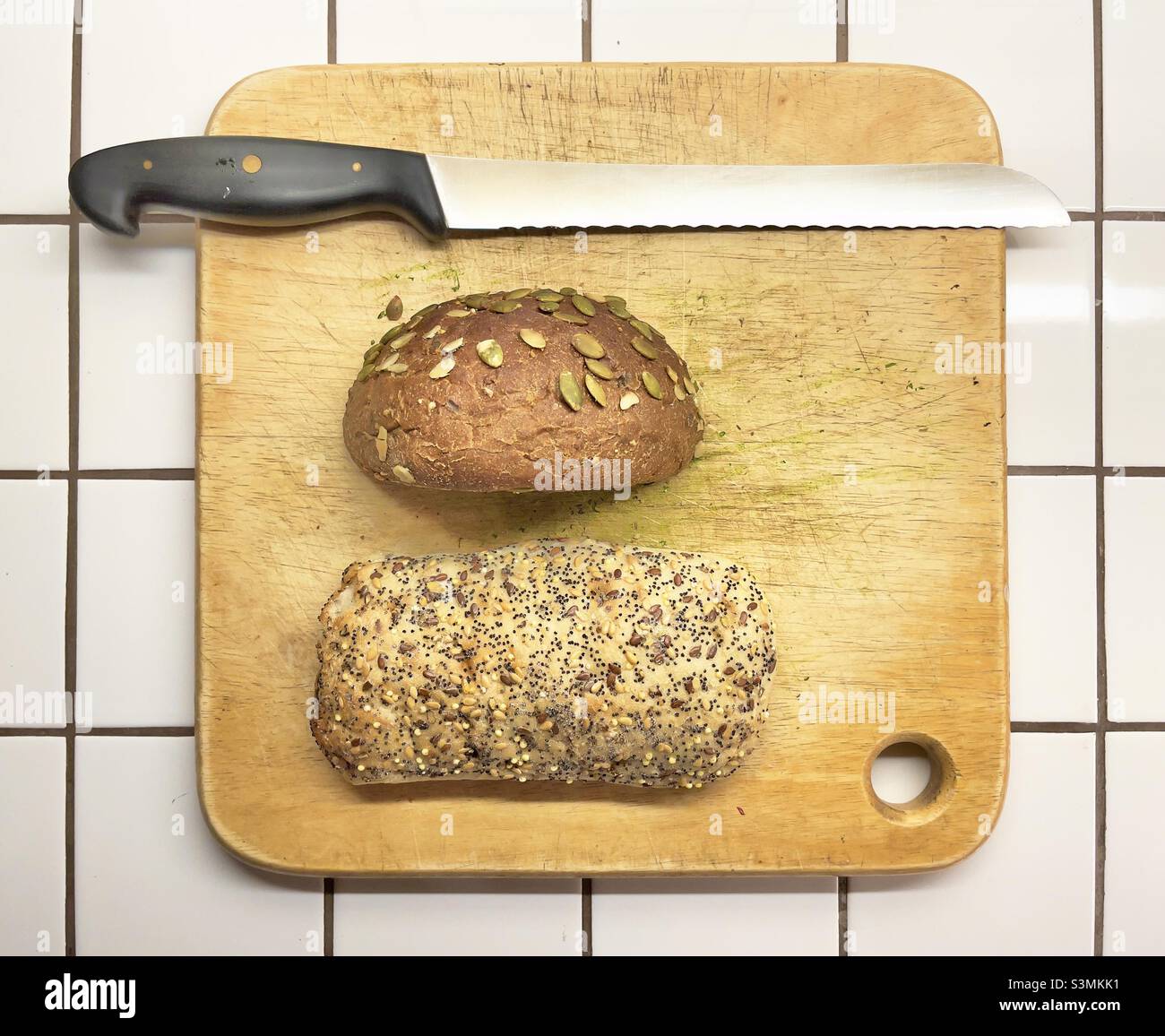 A breadboard with a knife and two kinds of brown seeded bread Stock Photo