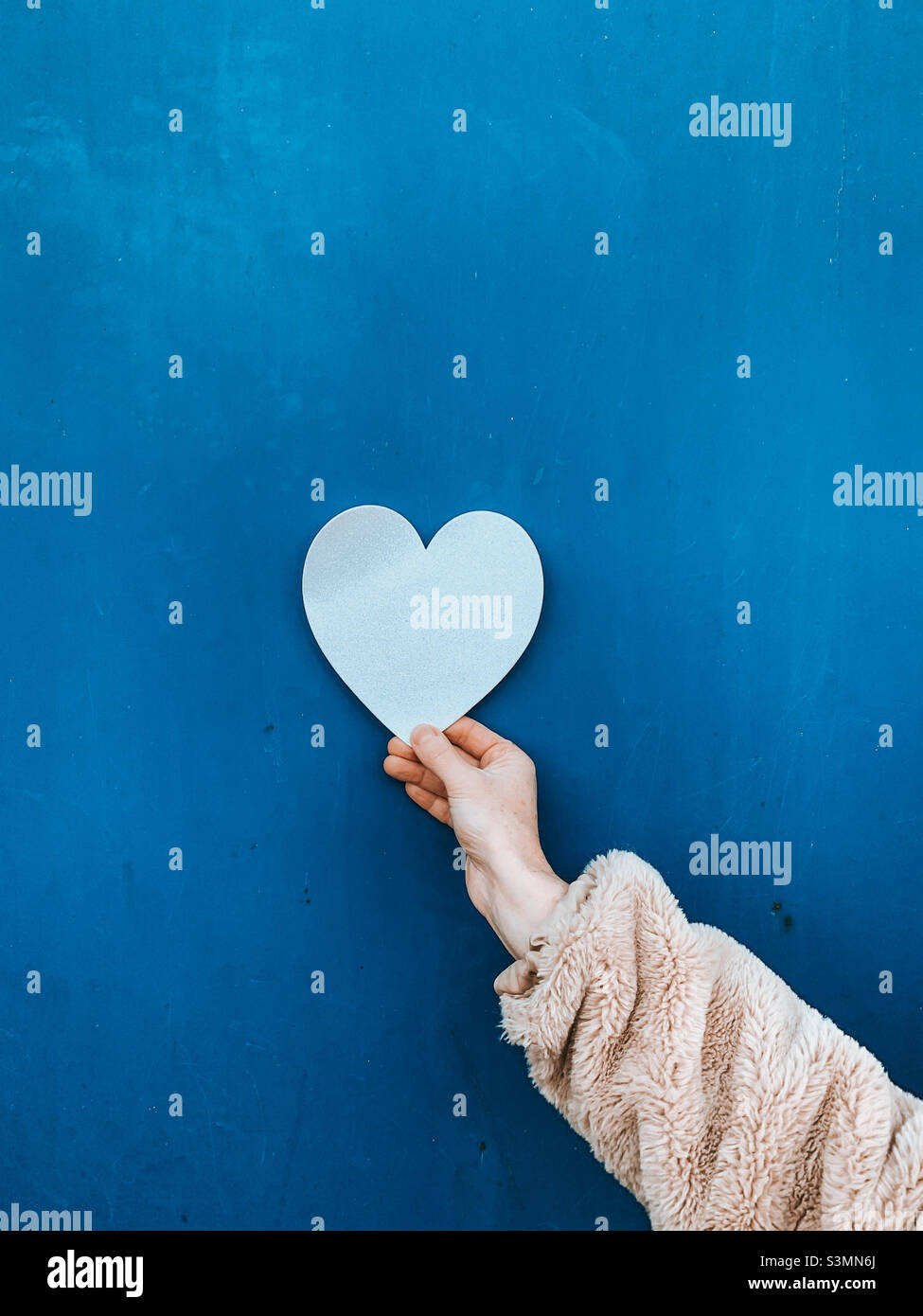 White Valentine’s Day card being held against a blue background - Smartphone Captured Stock Image