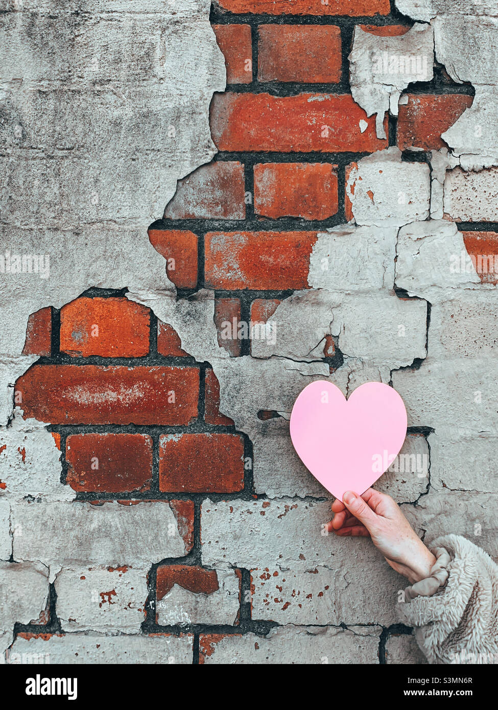 Pink Love heart card being held against a brick wall - Smartphone Captured Stock Image