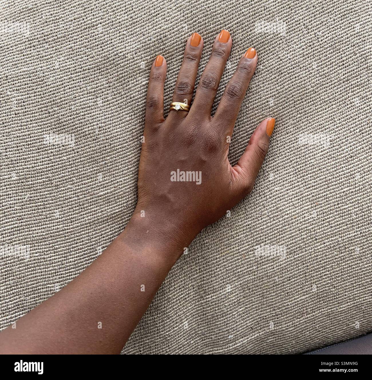 Brown skin hand with orange painted nails on a textured throw background Stock Photo