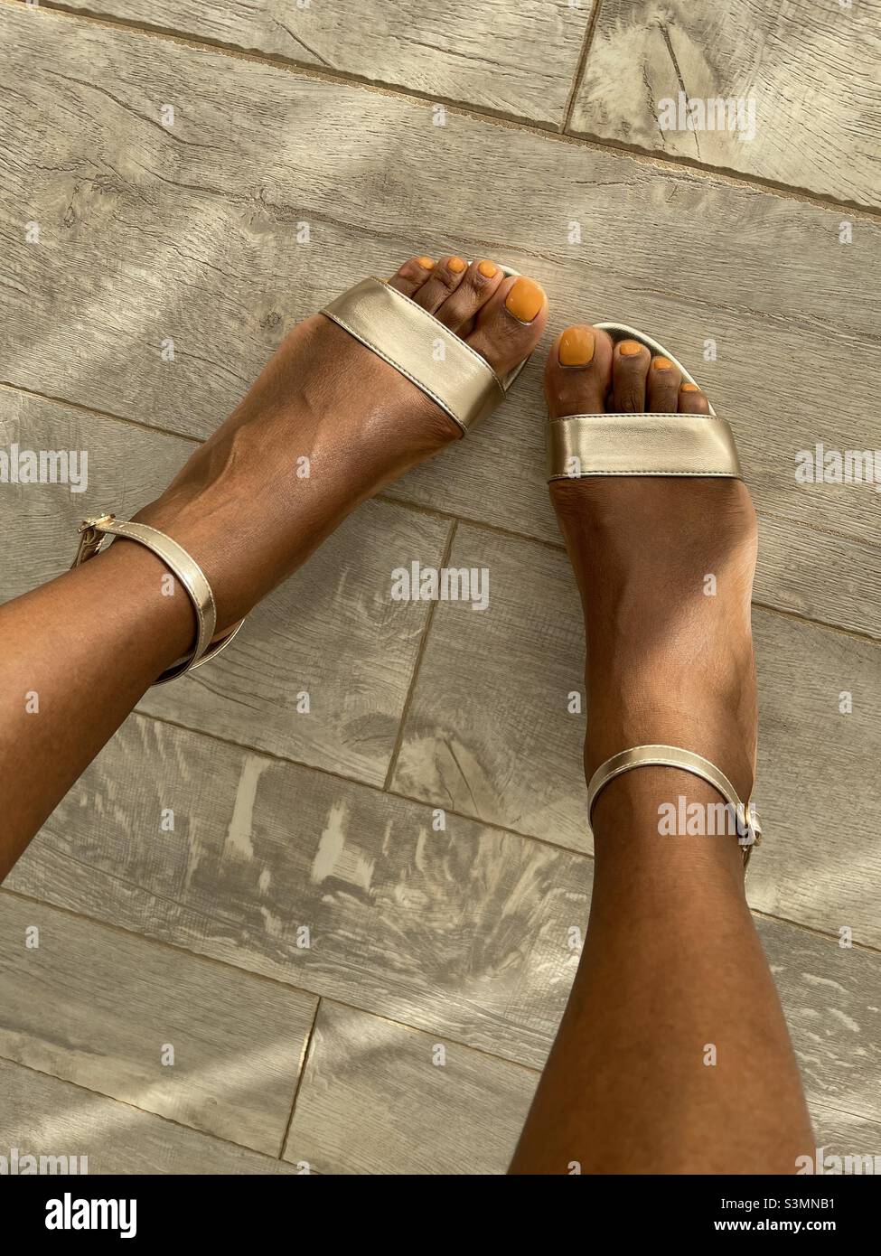 Brown skin girl, feet with mustard painted toe nails, sandals Stock Photo