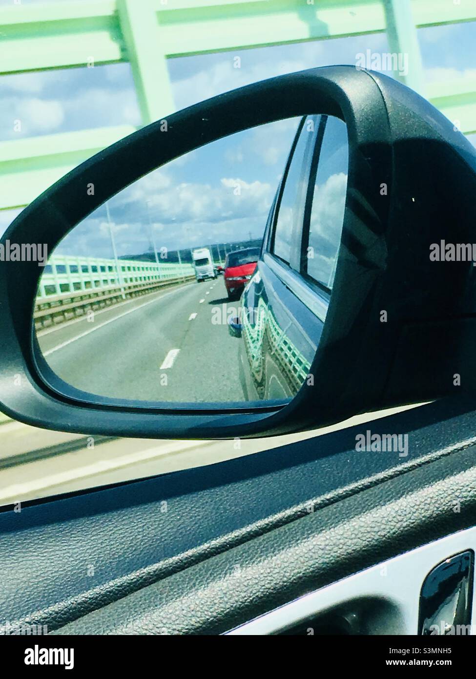 View of a car in the side mirror whilst crossing the second Severn bridge - also known as the Prince of Wales Bridge from England into Wales Stock Photo
