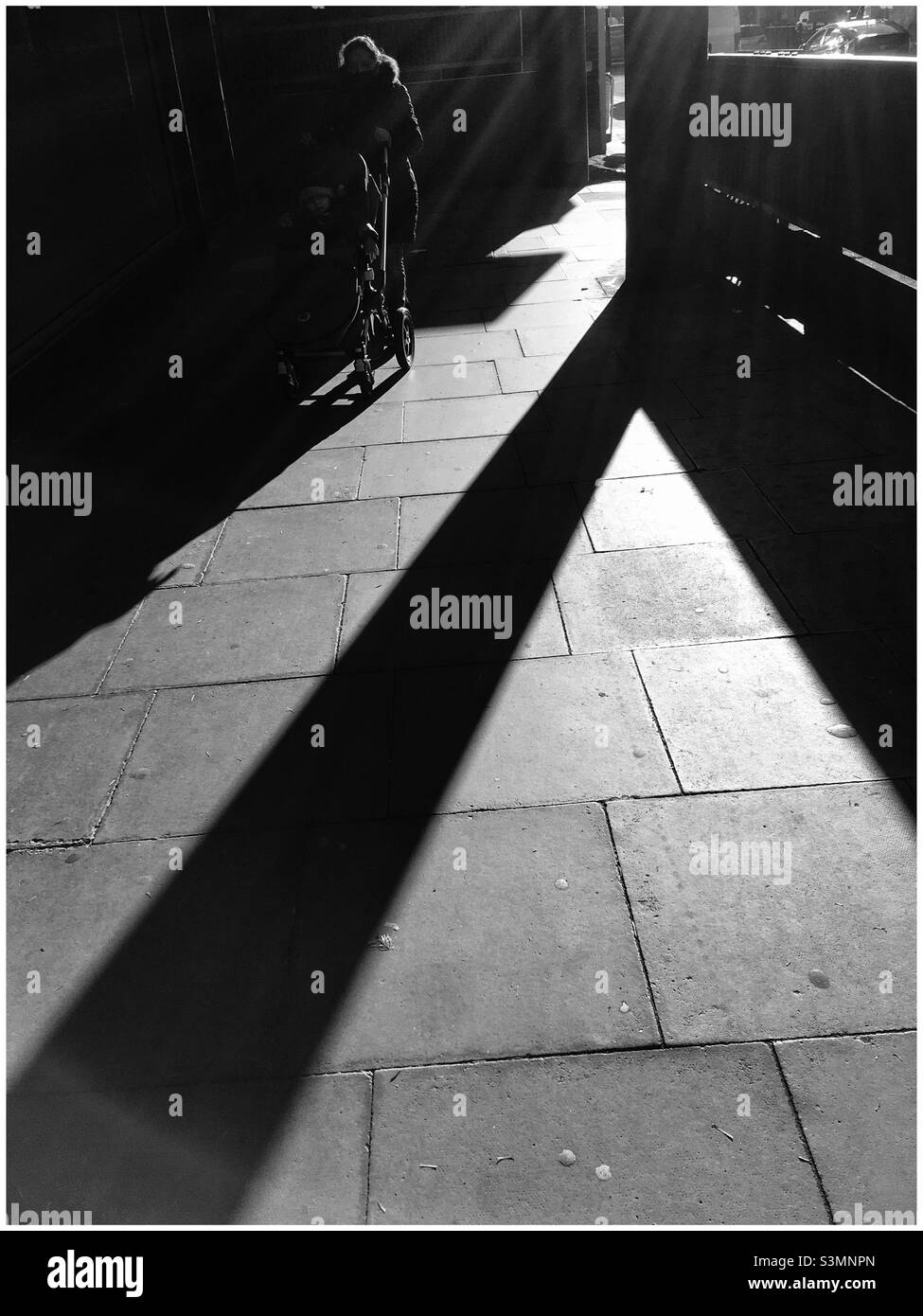Woman pushing baby in pram emerges from the shadows into a shaft of light - Smartphone Captured Stock Image