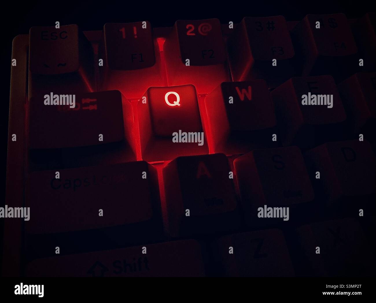 Keyboard with letter Q glowing in red. QAnon, conspiracy theory, internet, computer. Stock Photo