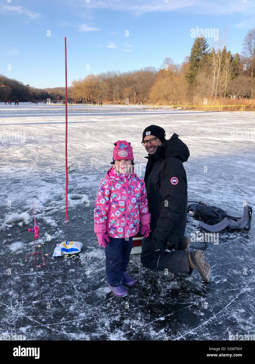 A father and daughter enjoying ice fishing on the frozen pond. - Smartphone Captured Stock Image