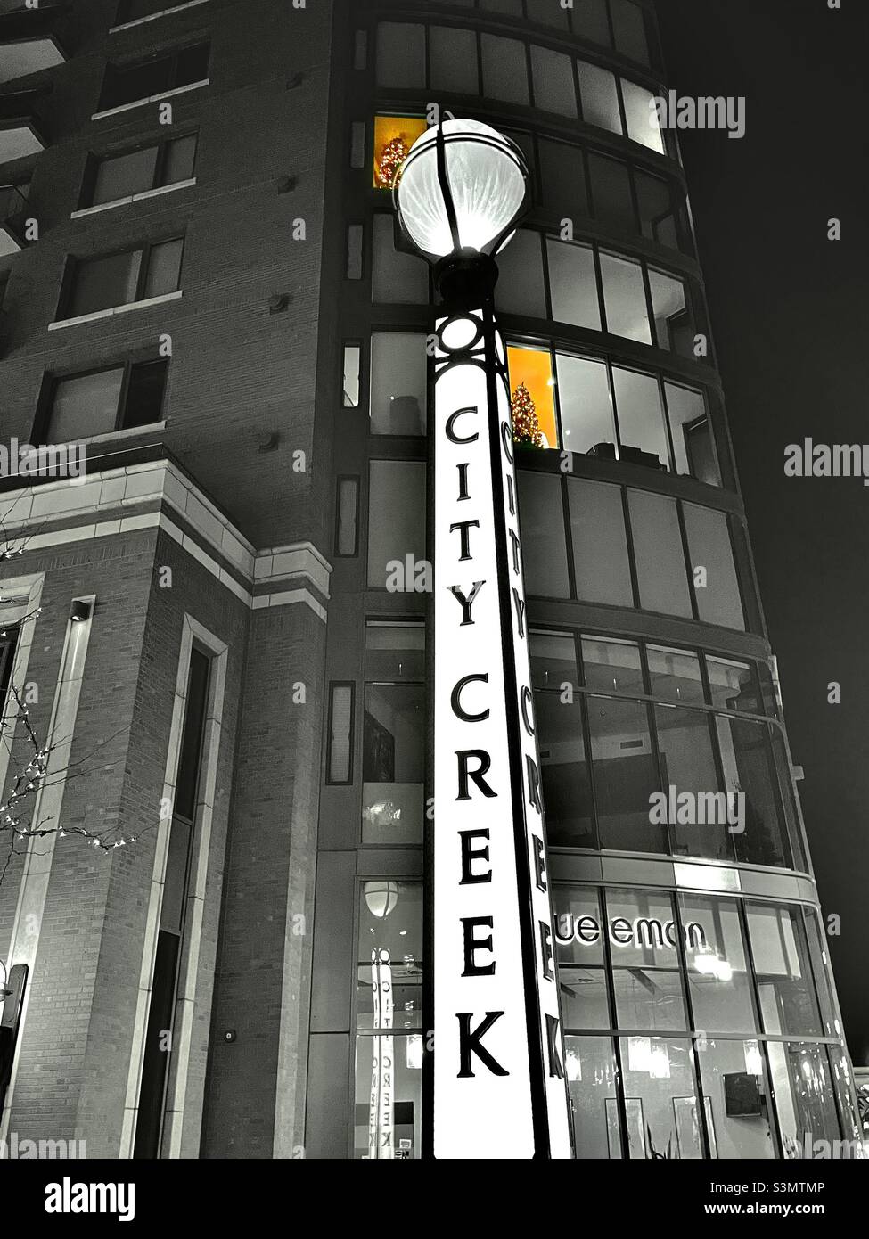 Looking up at an office building, next to the City Creek Center in downtown SLC, Utah during the holidays. A couple of lighted windows can be seen several floors up with decorated Christmas trees. - Smartphone Captured Stock Image