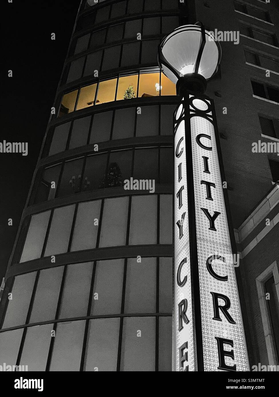 Looking up at an office building, next to the City Creek Center in downtown SLC, Utah during the holidays. A couple of lighted windows can be seen several floors up with decorated Christmas trees. - Smartphone Captured Stock Image