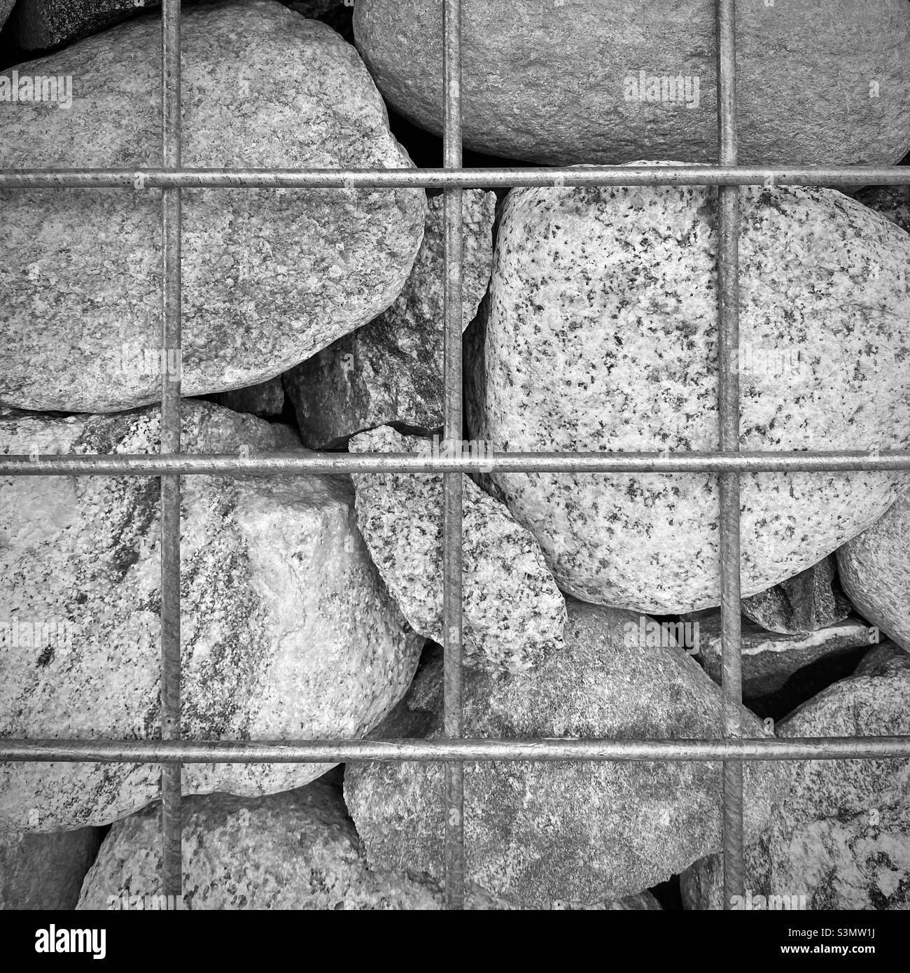 Grey rocks behind a metal wire mesh, creating abstract pattern, background for text and graphics Stock Photo