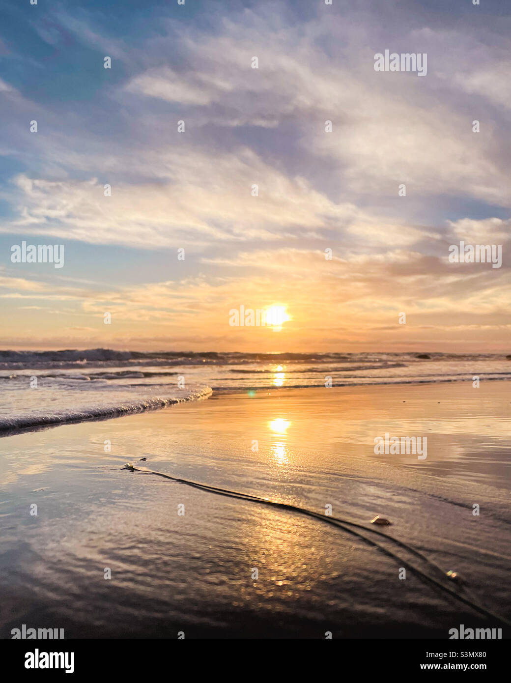Low angle view of setting sun from sandy beach with light reflecting in the water Stock Photo