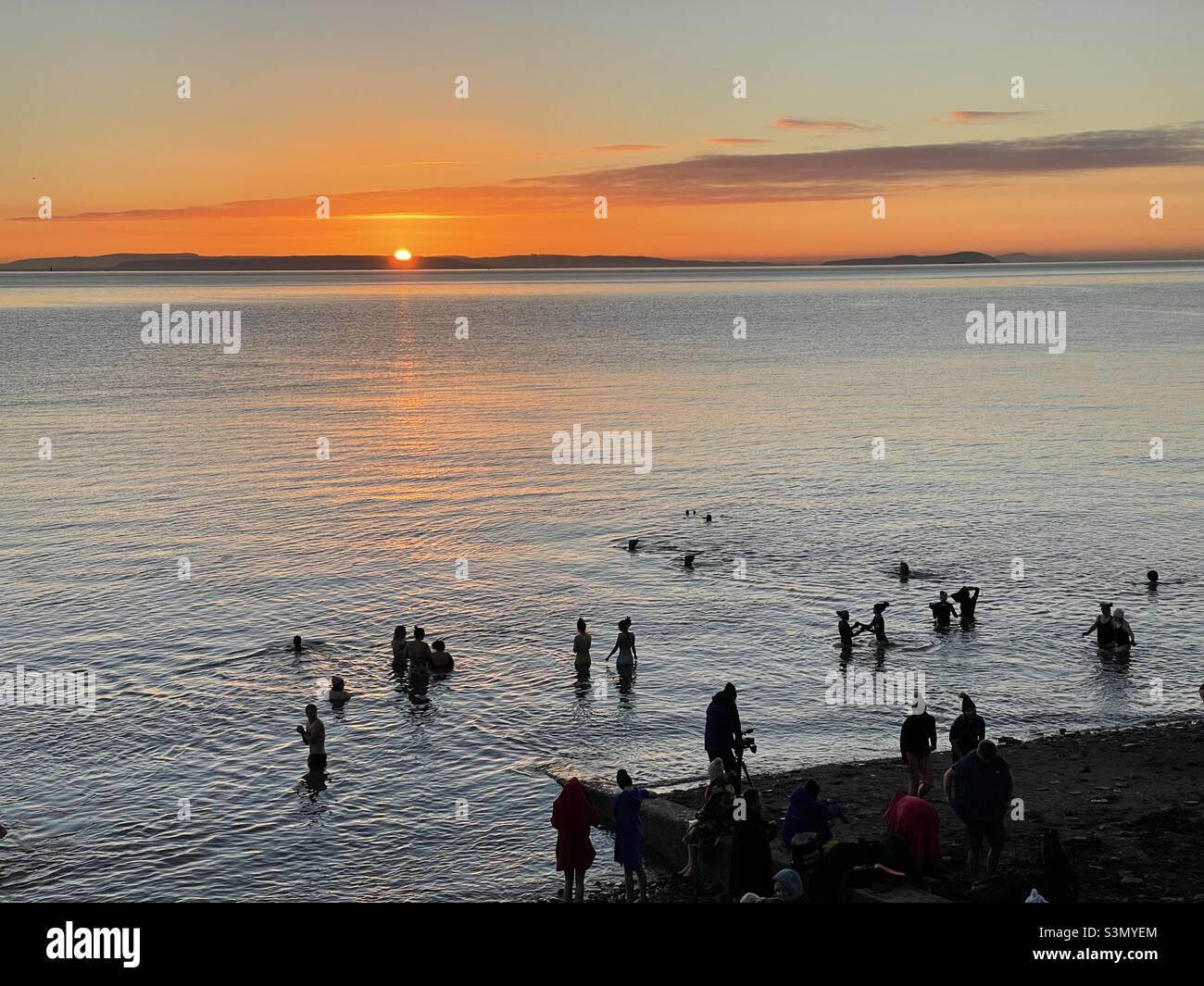 Dawn cold water swimmers at Penarth seafront in mid January, sunrise. Stock Photo