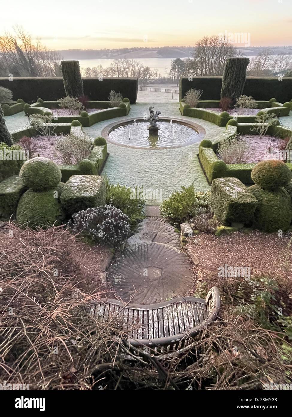 An early morning view of the parterre of a Rutland country house hotel, with frosted topiary, central water feature and a garden bench in the foreground - Smartphone Captured Stock Image