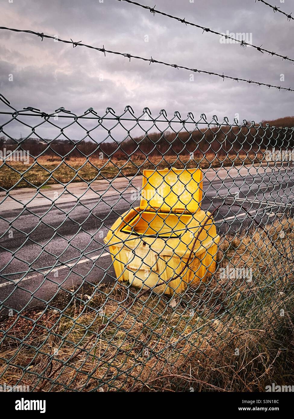 ‘Gritting on your own’ a lonely grit bin sits on abandoned ground, left exactly how it was when the fence went up Stock Photo