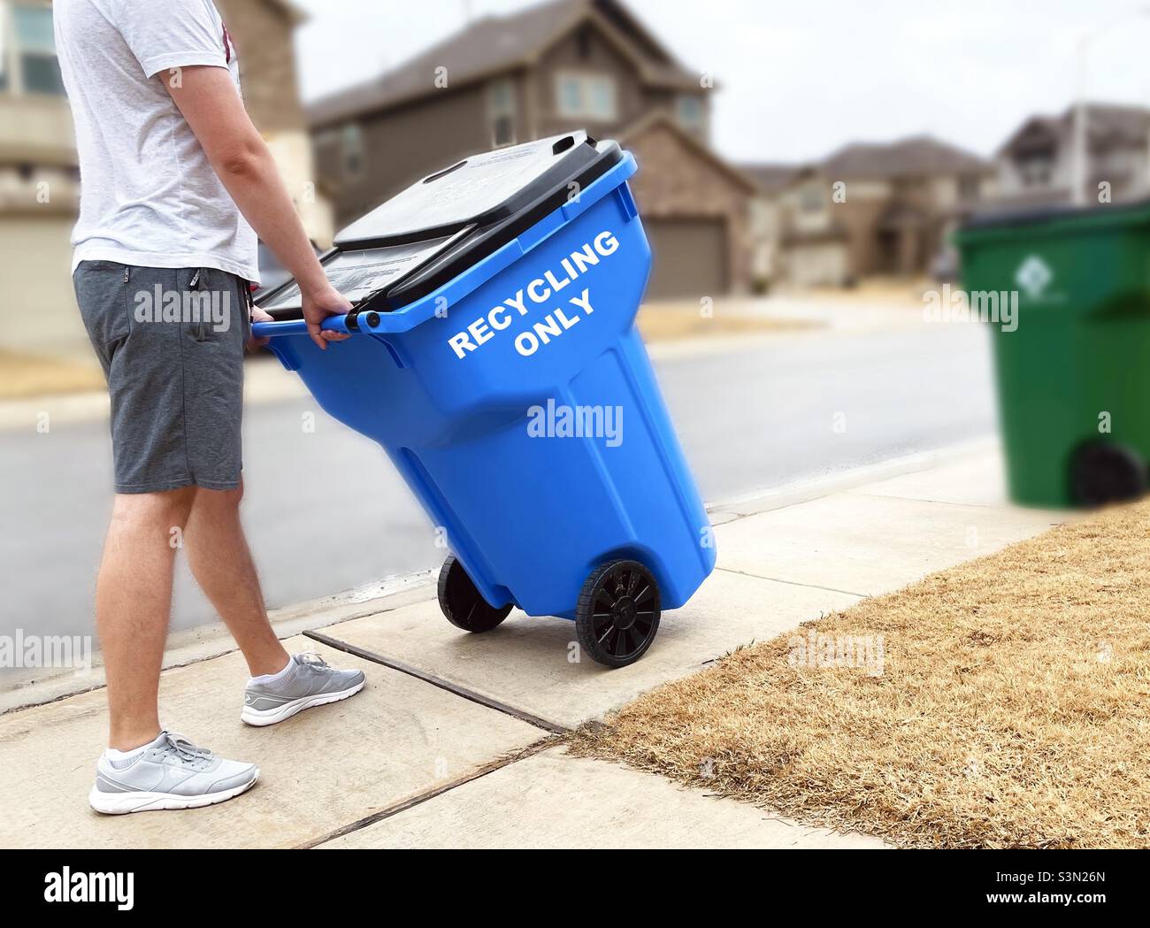 A man moving a trash can with recyclables along the road in the