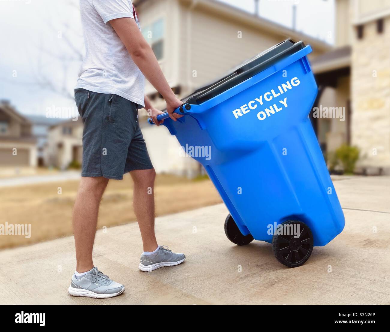 A man moving a trash can with recyclables at the front yard Stock Photo Alamy