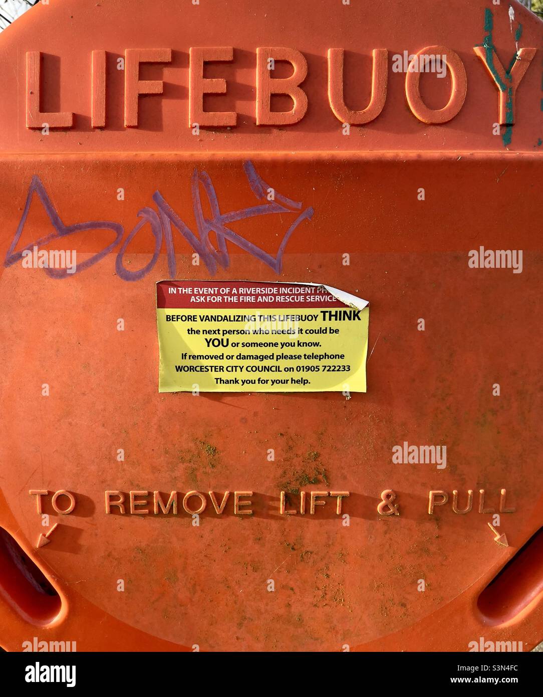 A plastic lifebuoy cover on the towpath of the river Severn in Worcester with graffiti and a sticker warning against vandalism - Smartphone Captured Stock Image