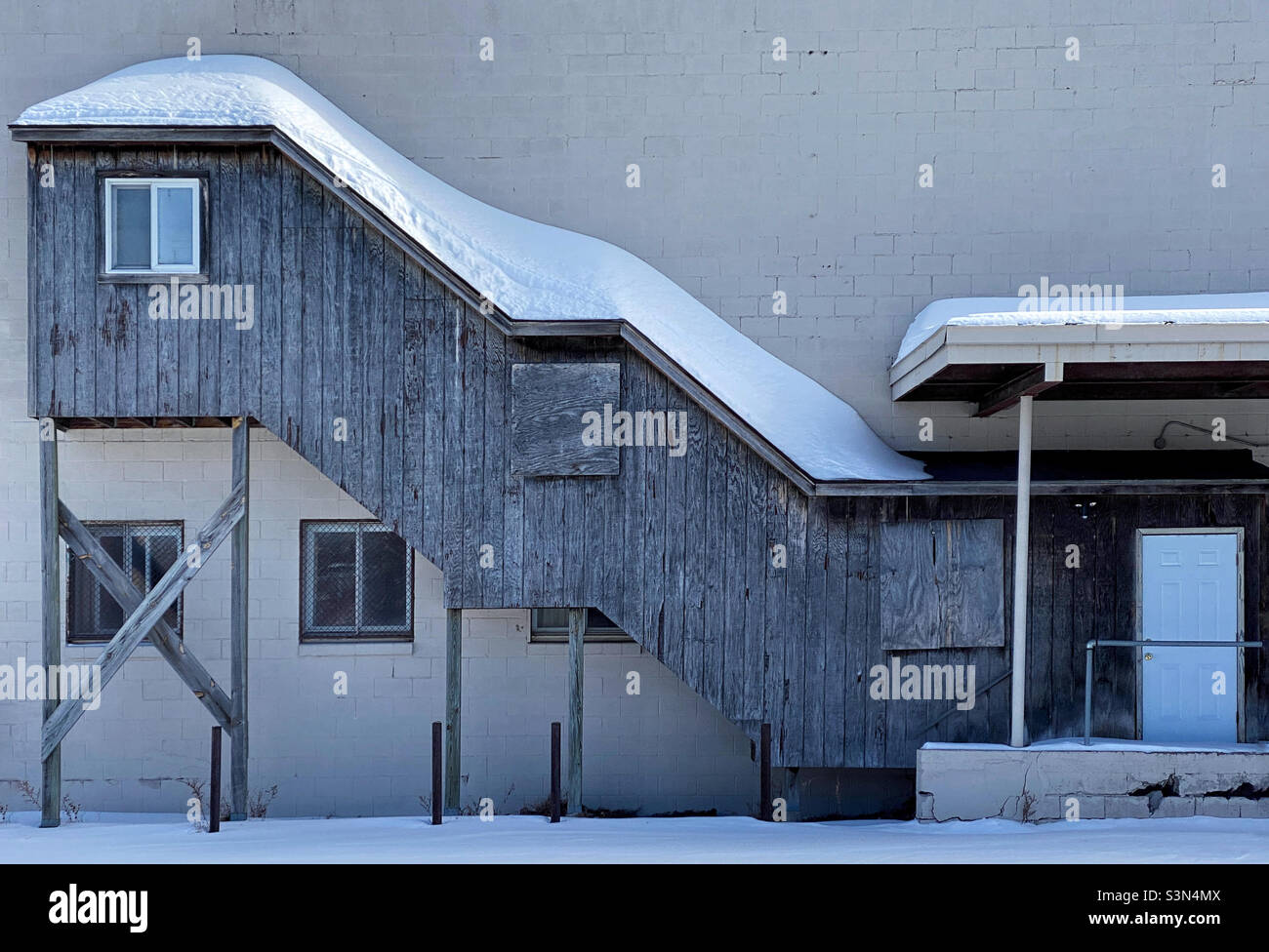 An enclosed staircase on the outside of a building with snow on the roof - Smartphone Captured Stock Image