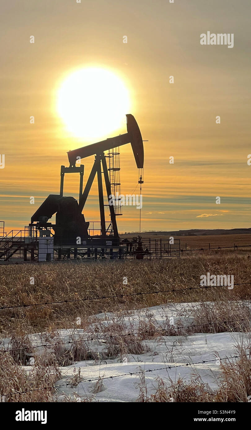An oil pumpjack silhouetted against the sun and golden winter morning sky. Near Calgary, Alberta, Canada. - Smartphone Captured Stock Image