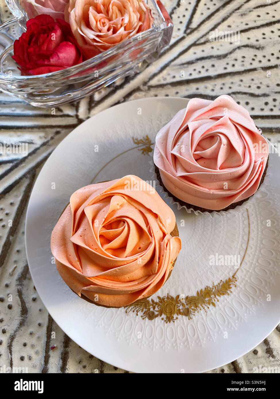 Two cupcakes on a china plate next to a heart shaped vase with real roses - Smartphone Captured Stock Image