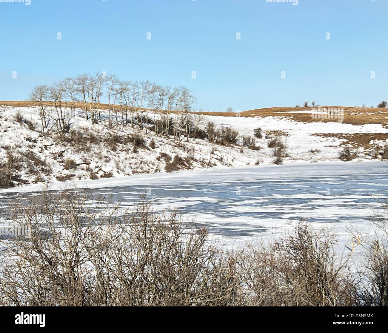 Pond partially covered in snow, starting to melt after a period of mild weather. Foothills, near Calgary, Alberta, Canada. Stock Photo