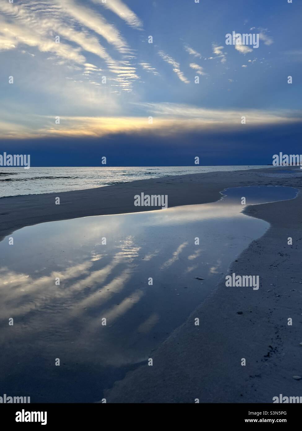 Dramatic sunset with cloud reflections onto beach sand Stock Photo