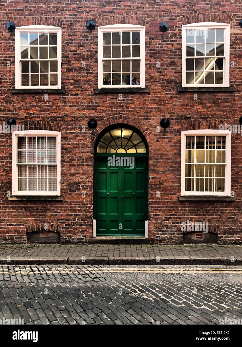 A grand old town house with large green door and sash windows on a cobbled street in a historic British city Stock Photo