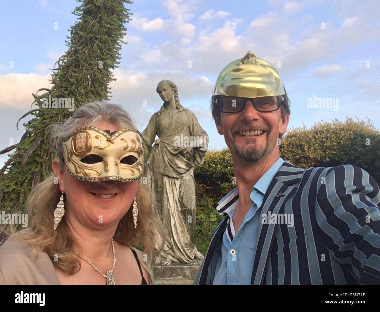 Couple at a masked ball in a formal garden with statue in the background Stock Photo