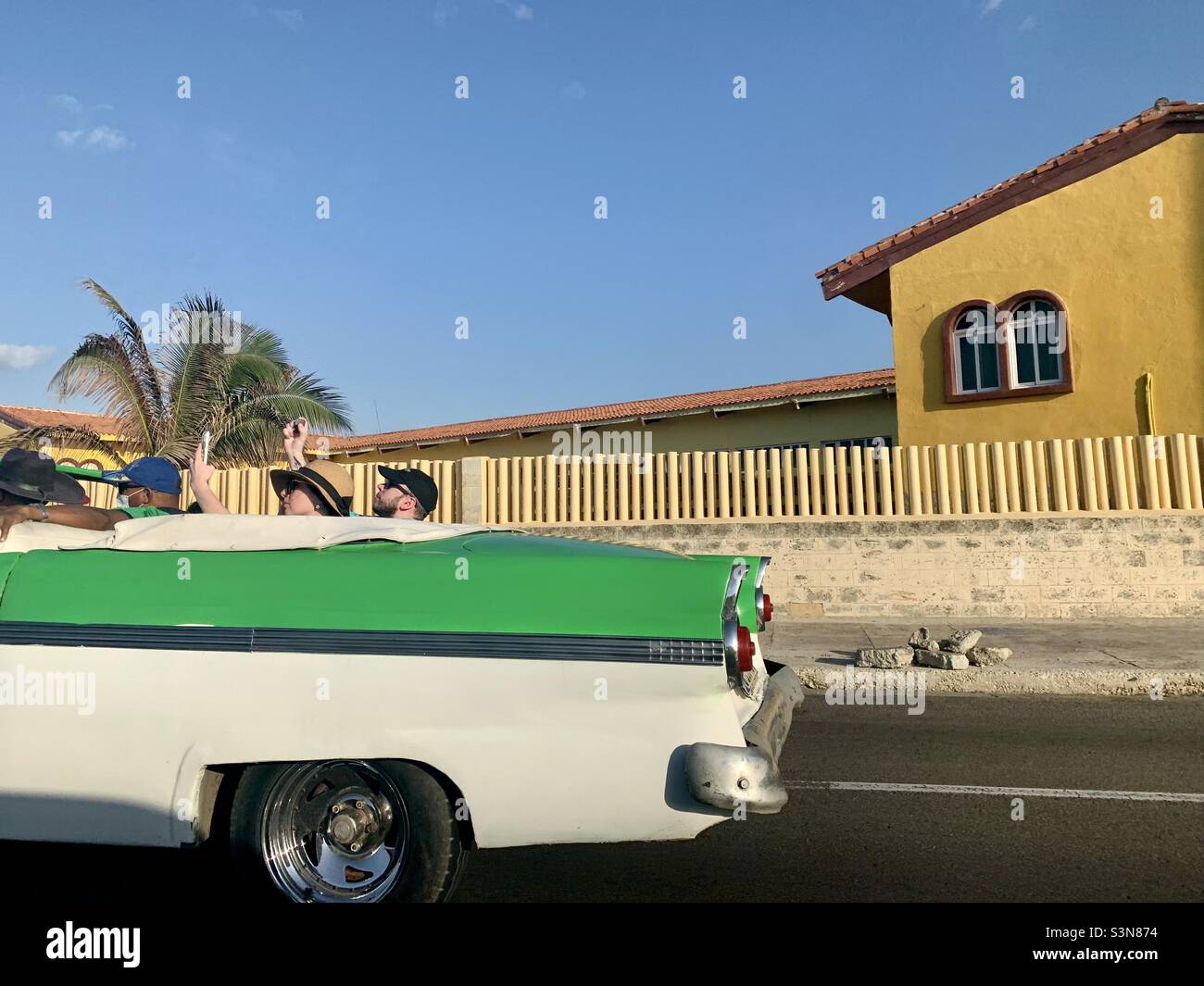 Two tourist in a convertible old timer take photos during their tour in Vedado, Havana, Cuba. Tourism industry in Cuba. Stock Photo