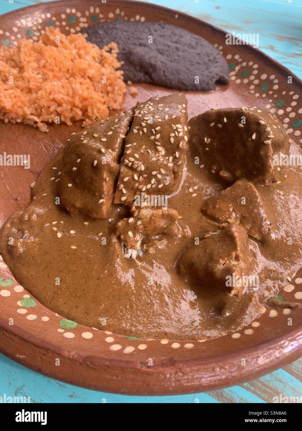 Chicken Mole dish with rice and beans on a Mexican handmade bowl with turquoise background table - Smartphone Captured Stock Image Chicken Mole dish with rice and beans on a Mexican handmade bowl with turquoise background table - Smartphone Captured Stock Image