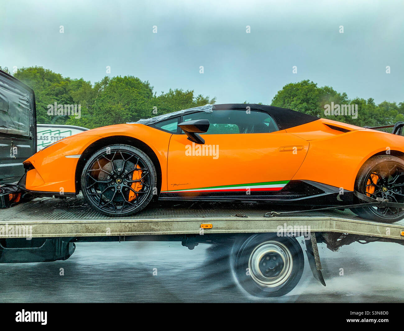 Lamborghini Huracan LP-640 Performante in orange on back of a trailer truck on motorway in rain - Smartphone Captured Stock Image